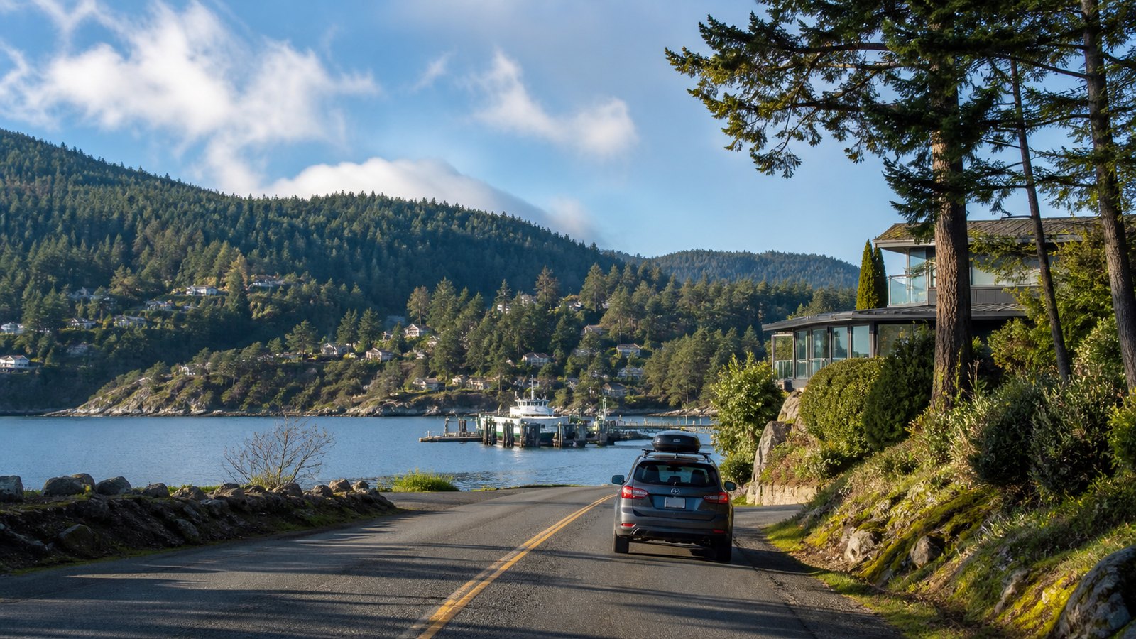 A coastal Sunshine Coast road leading toward water, homes, forest, and a ferry landing
